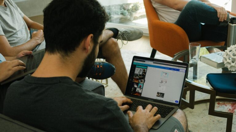 Three adults engage in digital collaboration with laptops in a modern office.